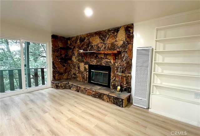 unfurnished living room with light wood-type flooring, a stone fireplace, and a heating unit