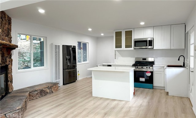 kitchen with appliances with stainless steel finishes, light countertops, glass insert cabinets, and white cabinetry