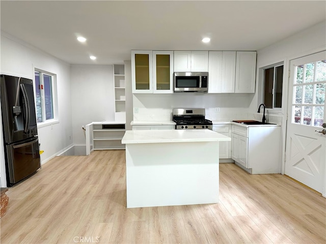 kitchen featuring a sink, a kitchen island, light countertops, appliances with stainless steel finishes, and glass insert cabinets