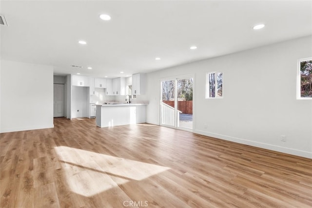 unfurnished living room with recessed lighting, visible vents, light wood-style flooring, a sink, and baseboards