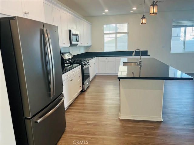 kitchen featuring dark countertops, appliances with stainless steel finishes, white cabinetry, pendant lighting, and a sink