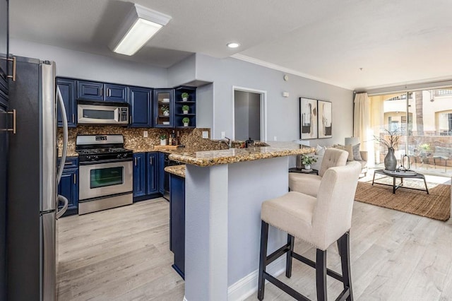 kitchen featuring a breakfast bar area, open shelves, appliances with stainless steel finishes, blue cabinets, and a peninsula