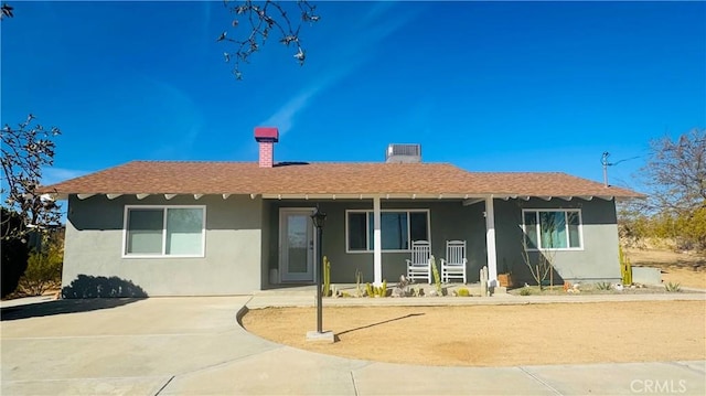 back of property featuring covered porch, a shingled roof, a chimney, and stucco siding