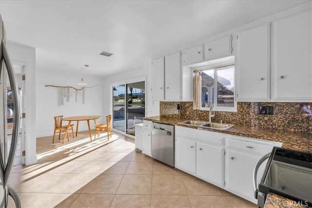 kitchen with light tile patterned flooring, a sink, white cabinetry, appliances with stainless steel finishes, and dark stone counters