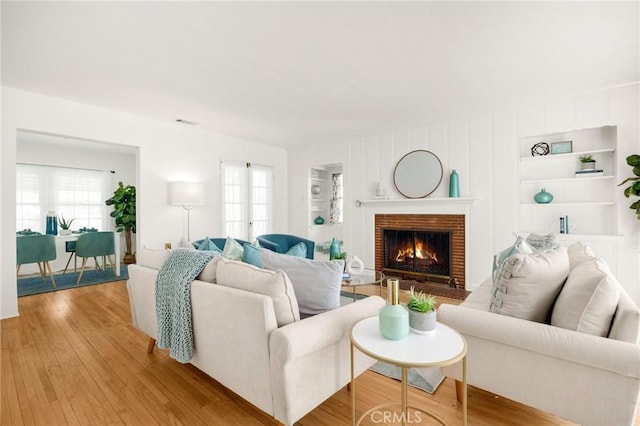 living room featuring light wood-type flooring, a brick fireplace, and built in shelves