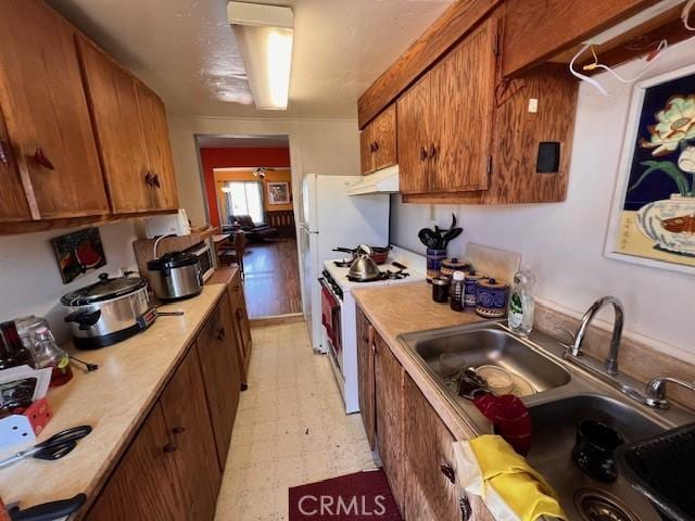 kitchen featuring under cabinet range hood, light countertops, white gas range oven, brown cabinets, and light floors