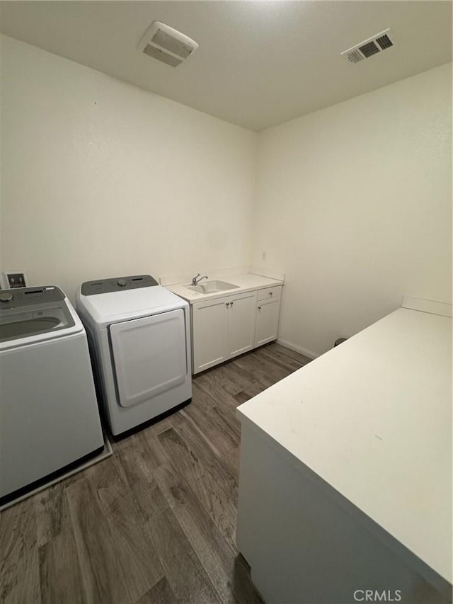 clothes washing area featuring visible vents, dark wood-type flooring, separate washer and dryer, cabinet space, and a sink