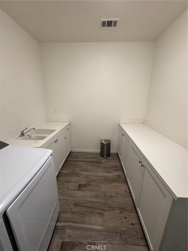 laundry area featuring visible vents, baseboards, dark wood-style floors, cabinet space, and a sink