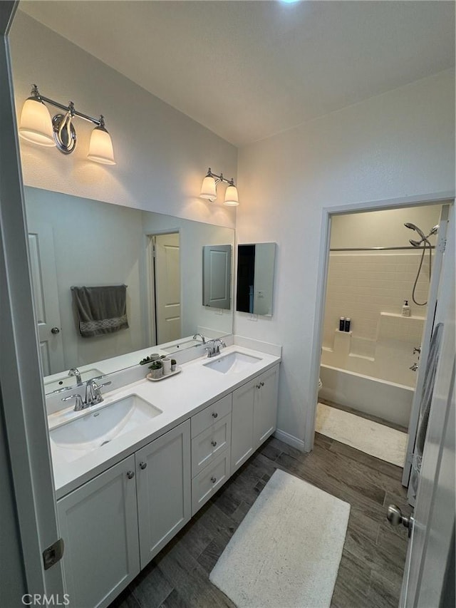 full bathroom with double vanity, wood finished floors, shower / bathtub combination, and a sink