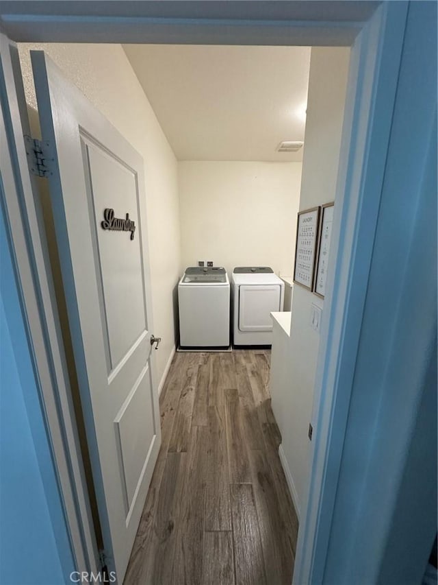 hallway with washing machine and clothes dryer, visible vents, baseboards, and wood finished floors