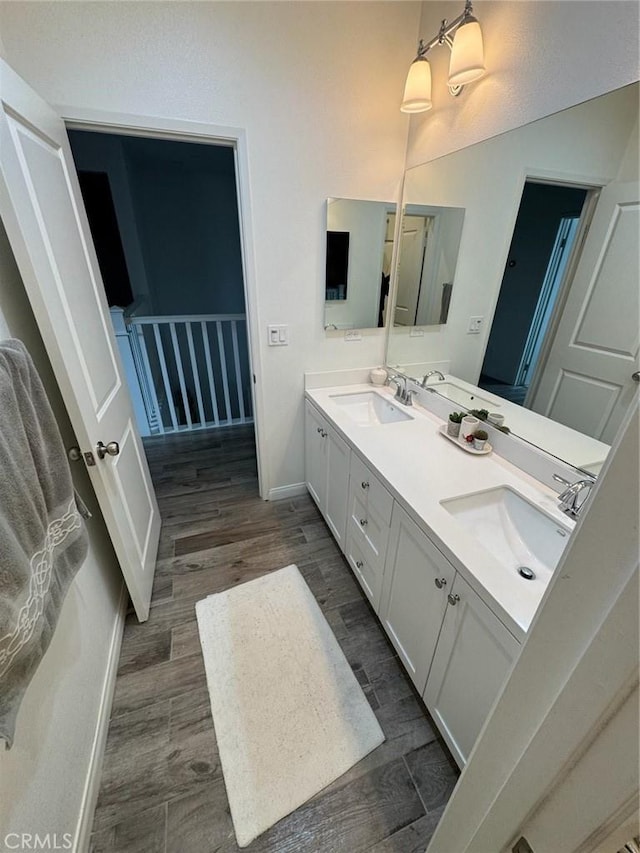 full bathroom featuring a sink, baseboards, wood finished floors, and double vanity