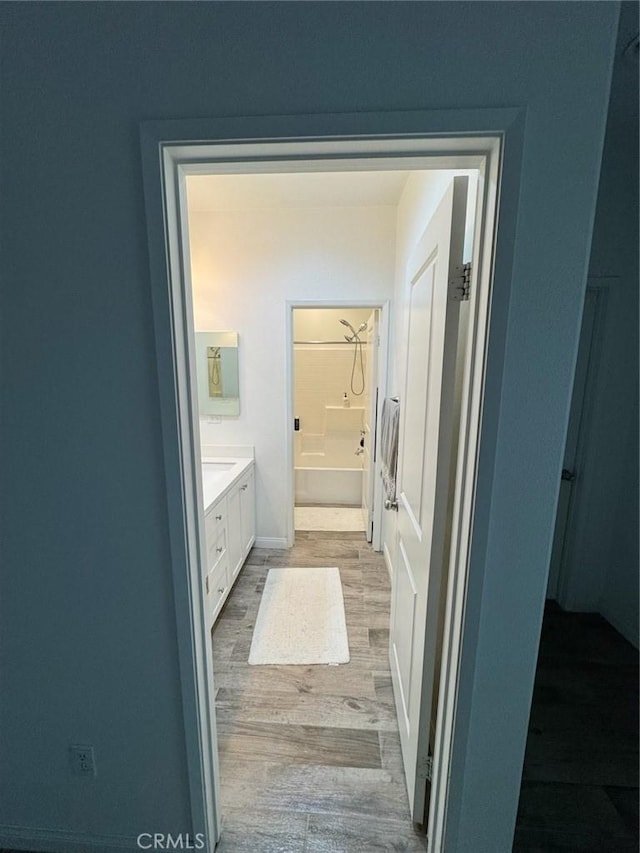 bathroom with baseboards, a bathing tub, wood finished floors, and vanity