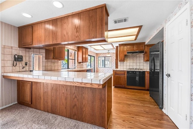 30220 Skippers Way Dr, Canyon Lake, CA 92587 - kitchen featuring tile countertops, under cabinet range hood, a peninsula, brown cabinets, and black appliances