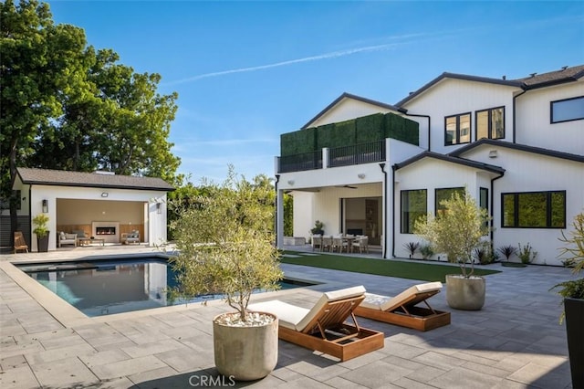 back of property featuring outdoor dining space, a patio area, an outdoor pool, and a balcony