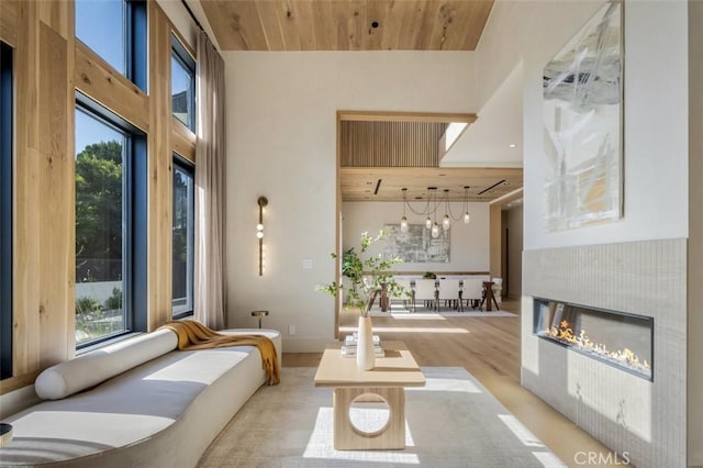 living area featuring a towering ceiling, light wood-style floors, wood ceiling, and a glass covered fireplace