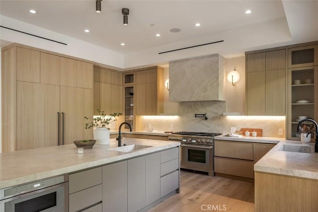 kitchen with stainless steel appliances, wall chimney range hood, modern cabinets, and a sink