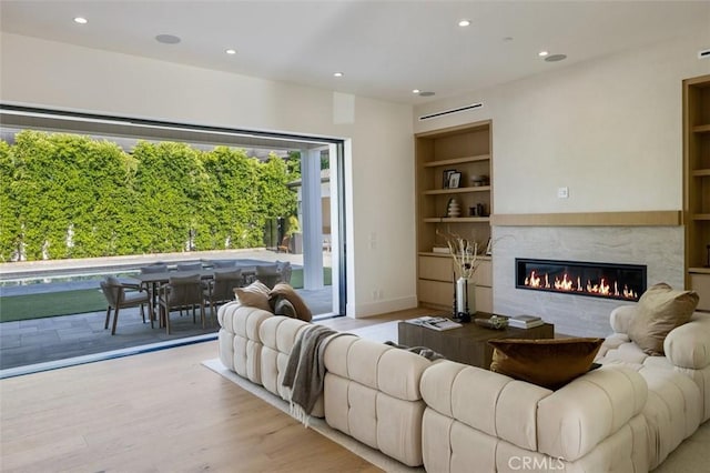 living room with light wood finished floors, recessed lighting, built in shelves, and a glass covered fireplace