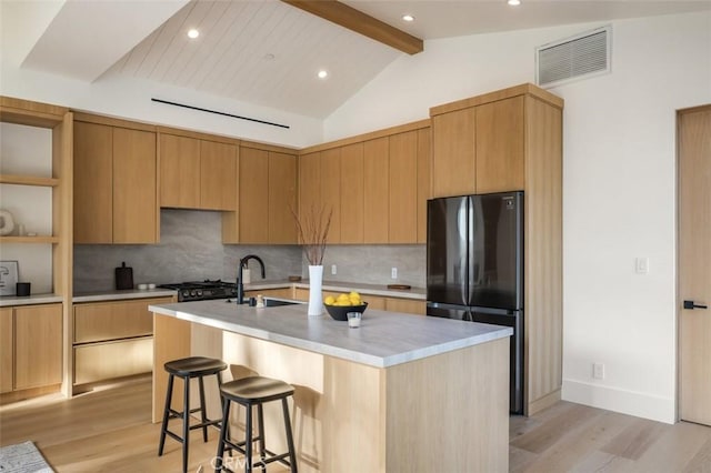 kitchen with light countertops, freestanding refrigerator, visible vents, and an island with sink