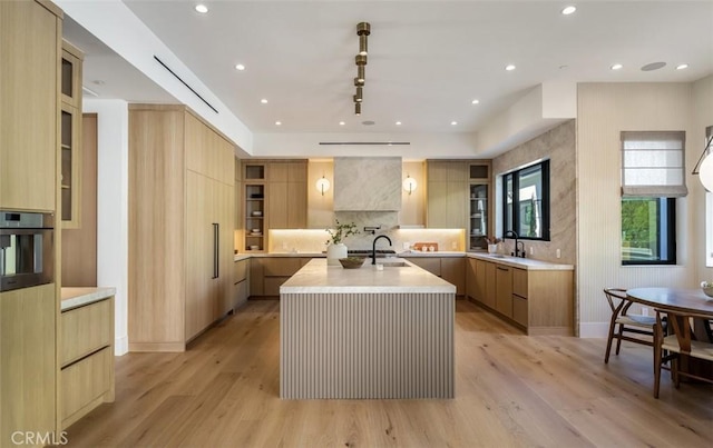 kitchen with light countertops, glass insert cabinets, modern cabinets, and a large island with sink