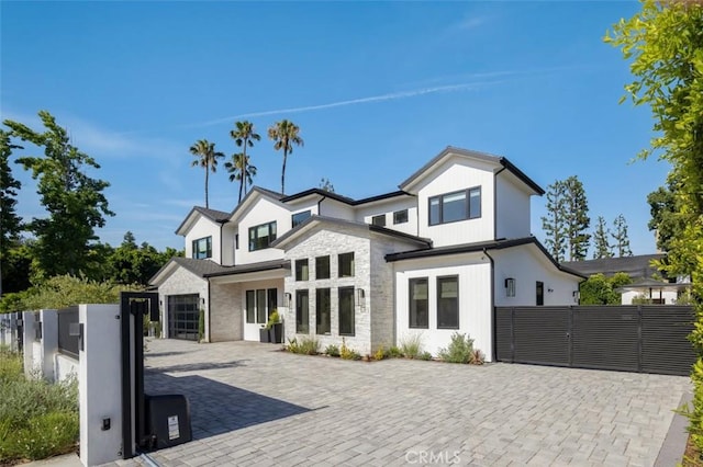 modern farmhouse with stone siding, decorative driveway, fence, and a gate