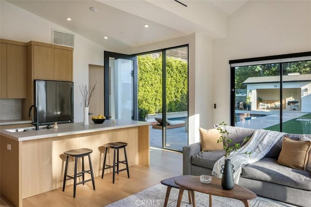 kitchen with open floor plan, a kitchen breakfast bar, refrigerator, vaulted ceiling, and light countertops