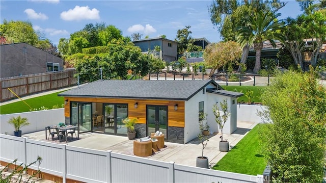 rear view of property with a shingled roof, a patio, stone siding, a fenced backyard, and french doors