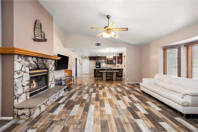 living room with dark wood-style flooring, a fireplace, visible vents, vaulted ceiling, and ceiling fan with notable chandelier