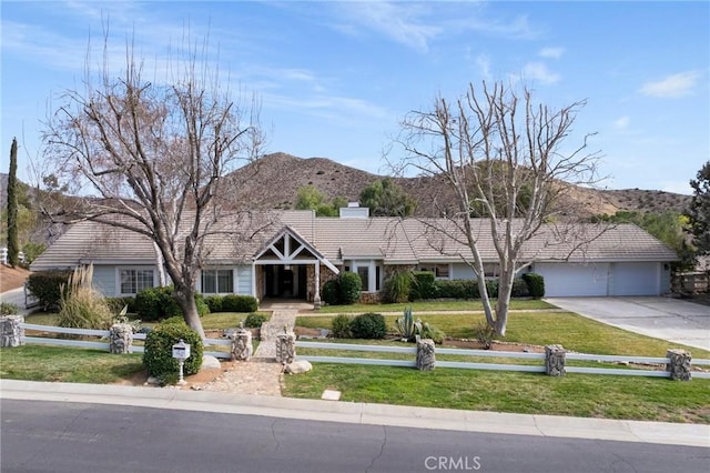 ranch-style house featuring concrete driveway, an attached garage, fence, a mountain view, and a front lawn