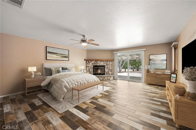 bedroom with access to outside, visible vents, a stone fireplace, and wood finished floors