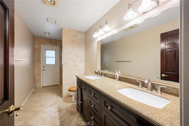 full bathroom featuring toilet, double vanity, tile walls, and a sink