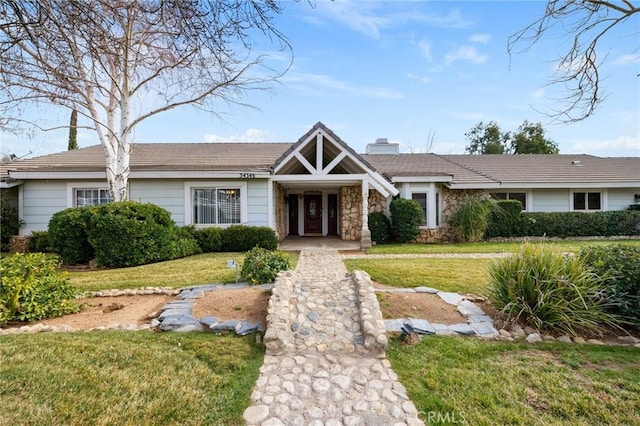 view of front of property with a front yard, stone siding, a tile roof, and a chimney