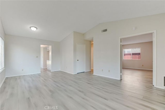 spare room with lofted ceiling, light wood-type flooring, visible vents, and baseboards