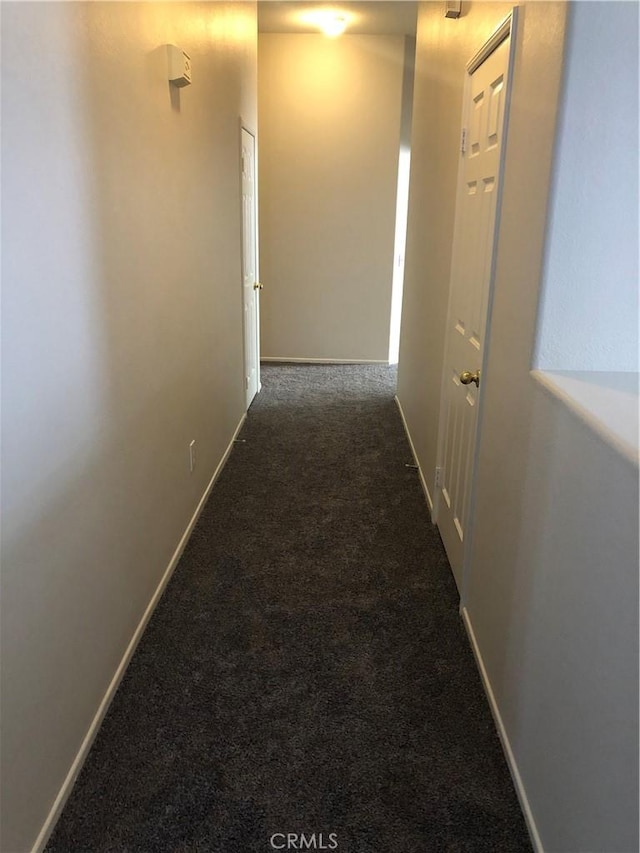 hallway featuring baseboards and dark carpet