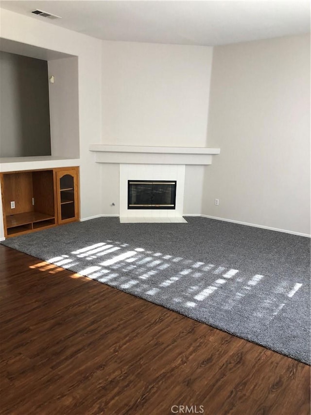 unfurnished living room with baseboards, visible vents, wood finished floors, and a tile fireplace