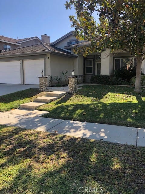 view of front of house featuring an attached garage, a chimney, a front lawn, and stucco siding