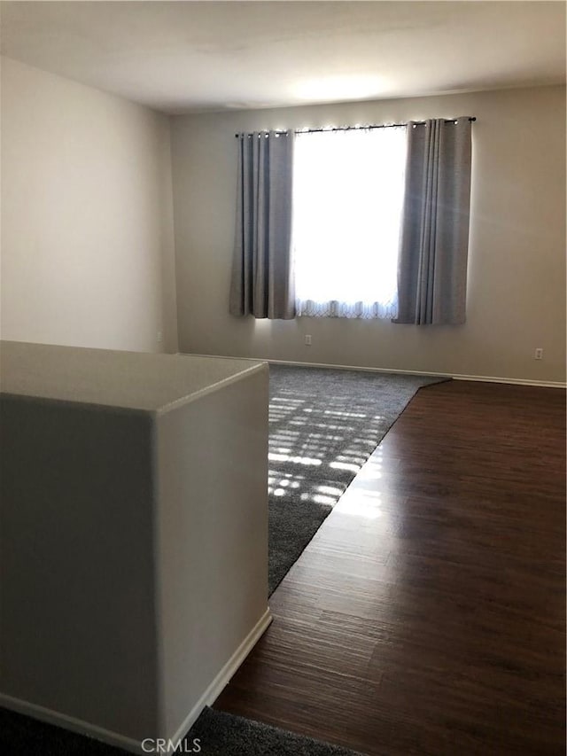 unfurnished room featuring dark wood-type flooring and baseboards