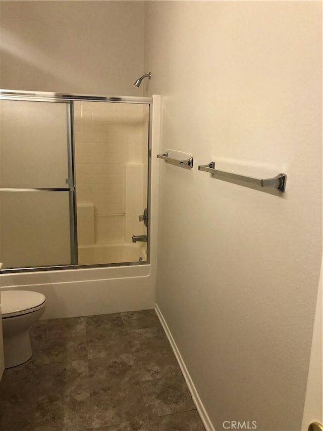 bathroom featuring toilet, enclosed tub / shower combo, and baseboards