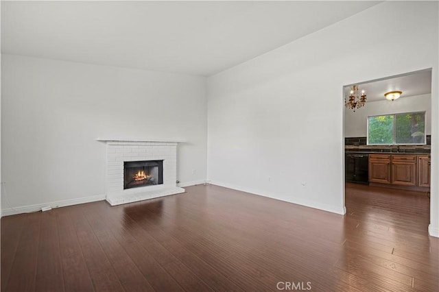 unfurnished living room featuring dark wood-style floors, a brick fireplace, a sink, a chandelier, and baseboards