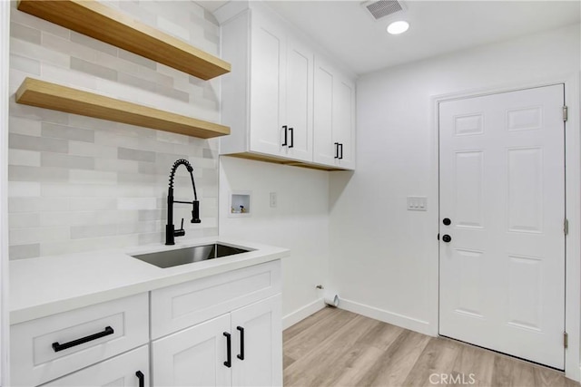 clothes washing area featuring cabinet space, visible vents, hookup for a washing machine, light wood-style floors, and a sink