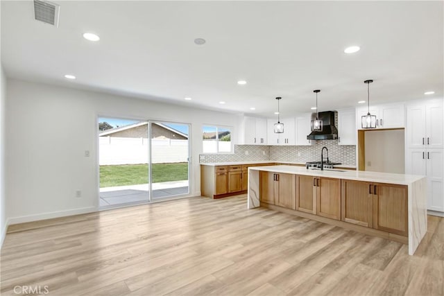 kitchen with wall chimney range hood, a large island, white cabinets, and light countertops