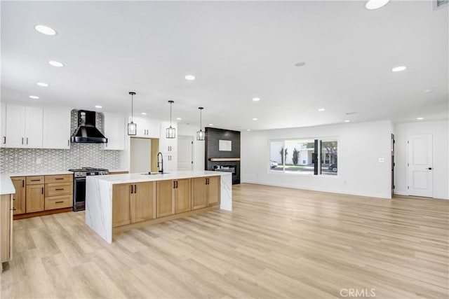 kitchen with stainless steel stove, open floor plan, white cabinetry, a large island with sink, and wall chimney exhaust hood