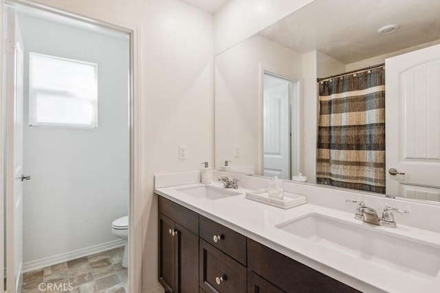 bathroom featuring toilet, double vanity, baseboards, and a sink