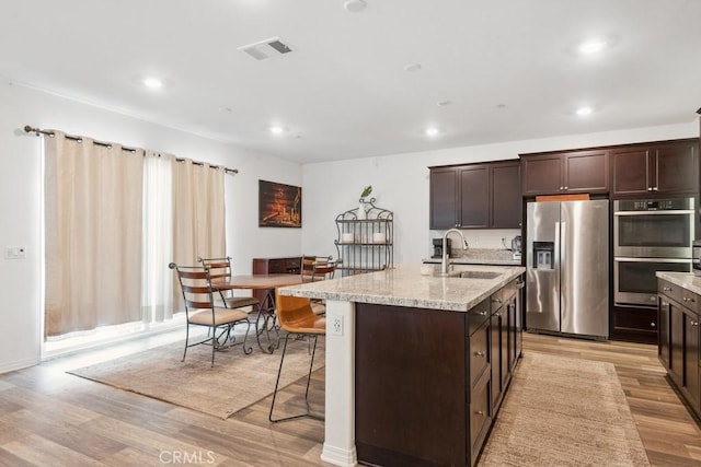 kitchen featuring stainless steel appliances, a sink, light wood finished floors, and an island with sink