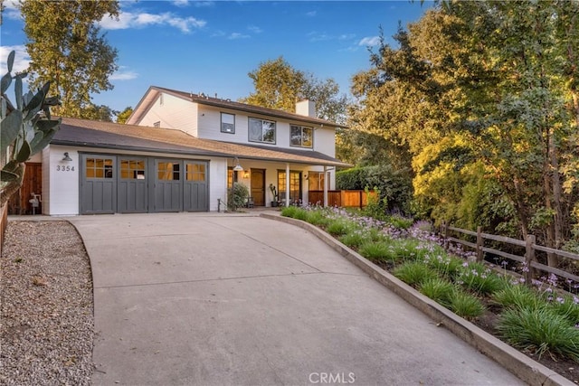 view of front of home with a garage, concrete driveway, a chimney, and fence