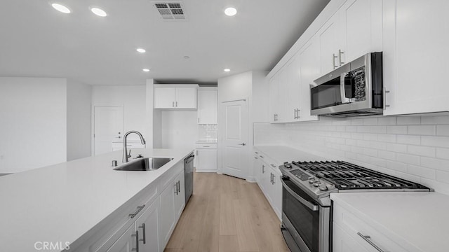 kitchen featuring visible vents, white cabinets, appliances with stainless steel finishes, light wood-style floors, and a sink