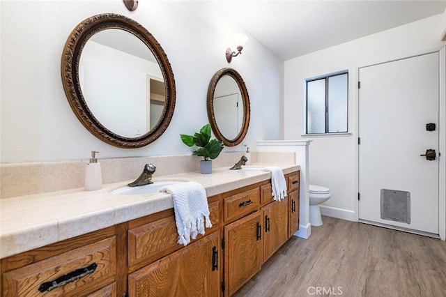 bathroom with double vanity, a sink, toilet, and wood finished floors