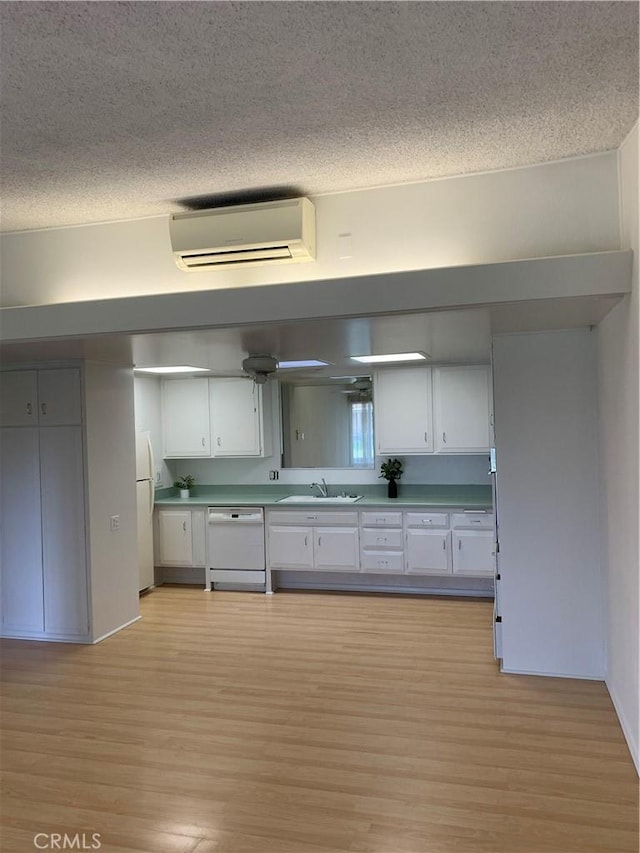 kitchen featuring white appliances, a textured ceiling, an AC wall unit, light wood-type flooring, and white cabinetry