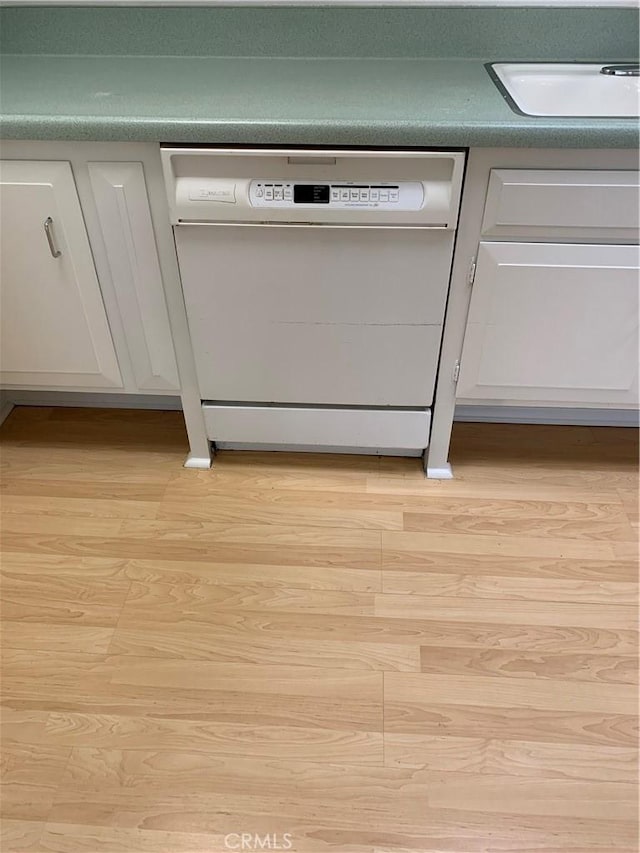 interior details with white cabinetry, white dishwasher, light wood finished floors, and a sink