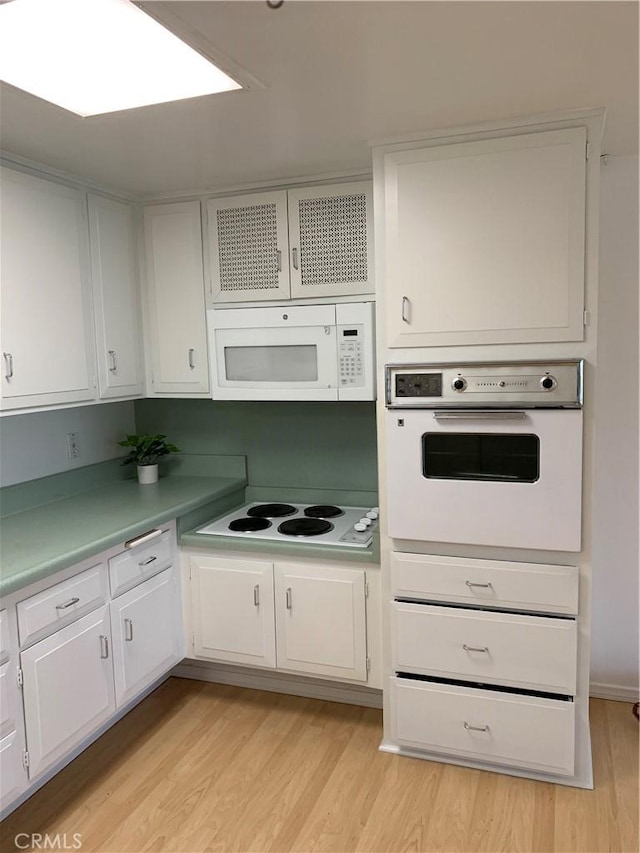 kitchen with light wood-type flooring, light countertops, white appliances, and white cabinetry