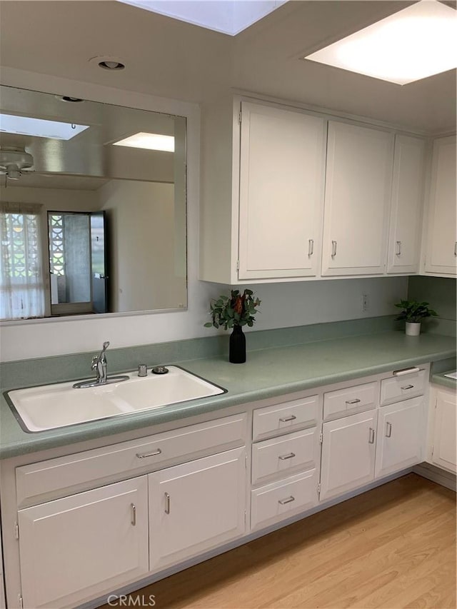 kitchen with a sink, light wood-style flooring, white cabinets, and light countertops